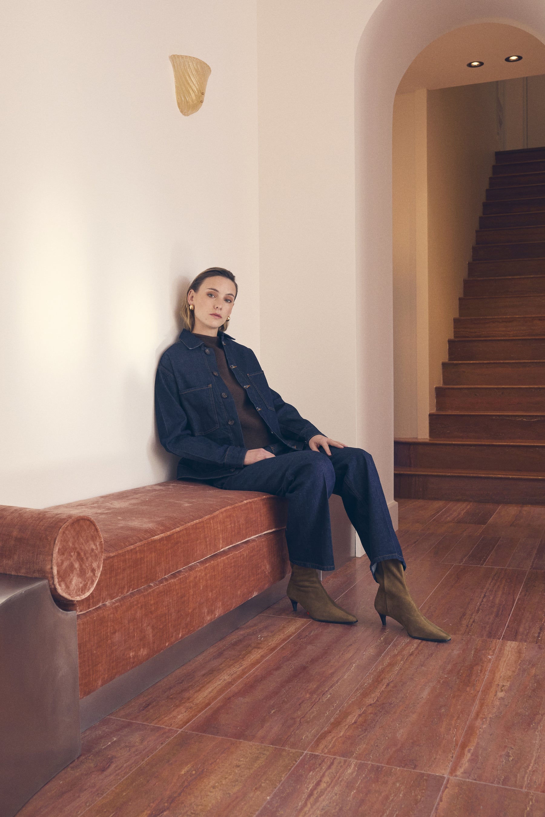 Woman sitting on a red bench in a modern interior setting with wooden floor and staircase.
