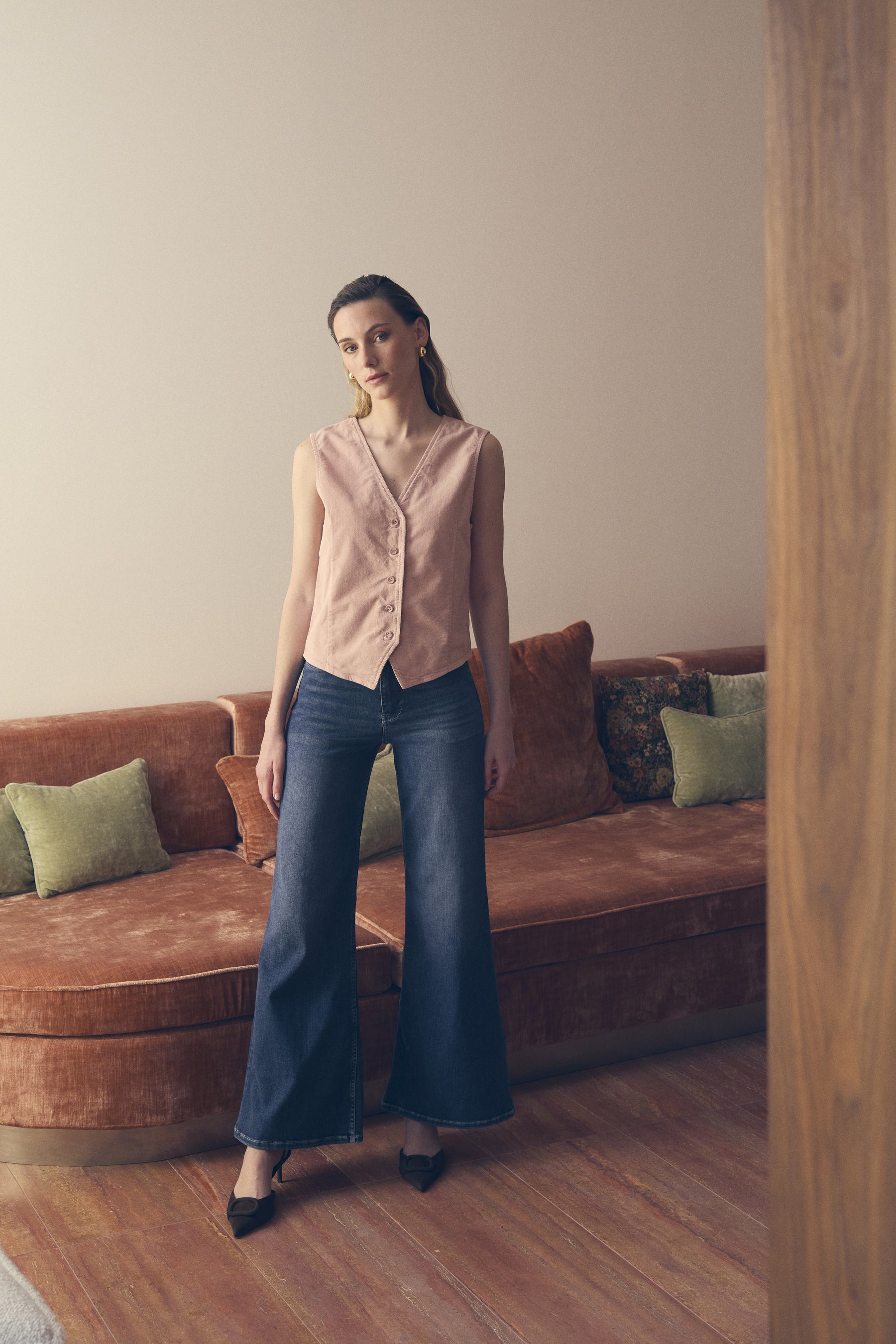 Woman standing in a living room with a brown sofa and green pillows.