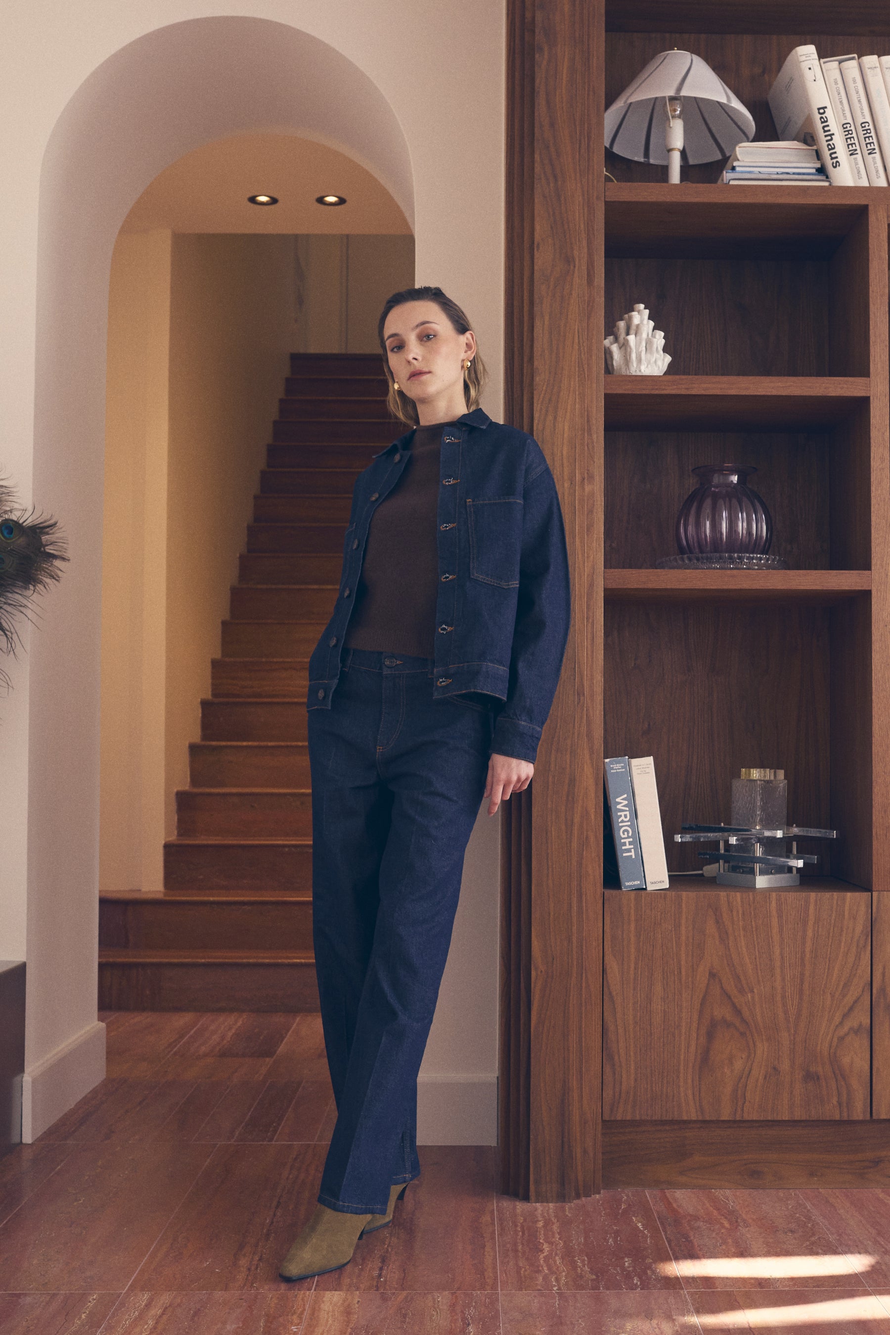 Woman standing in a room with wooden shelves and a staircase