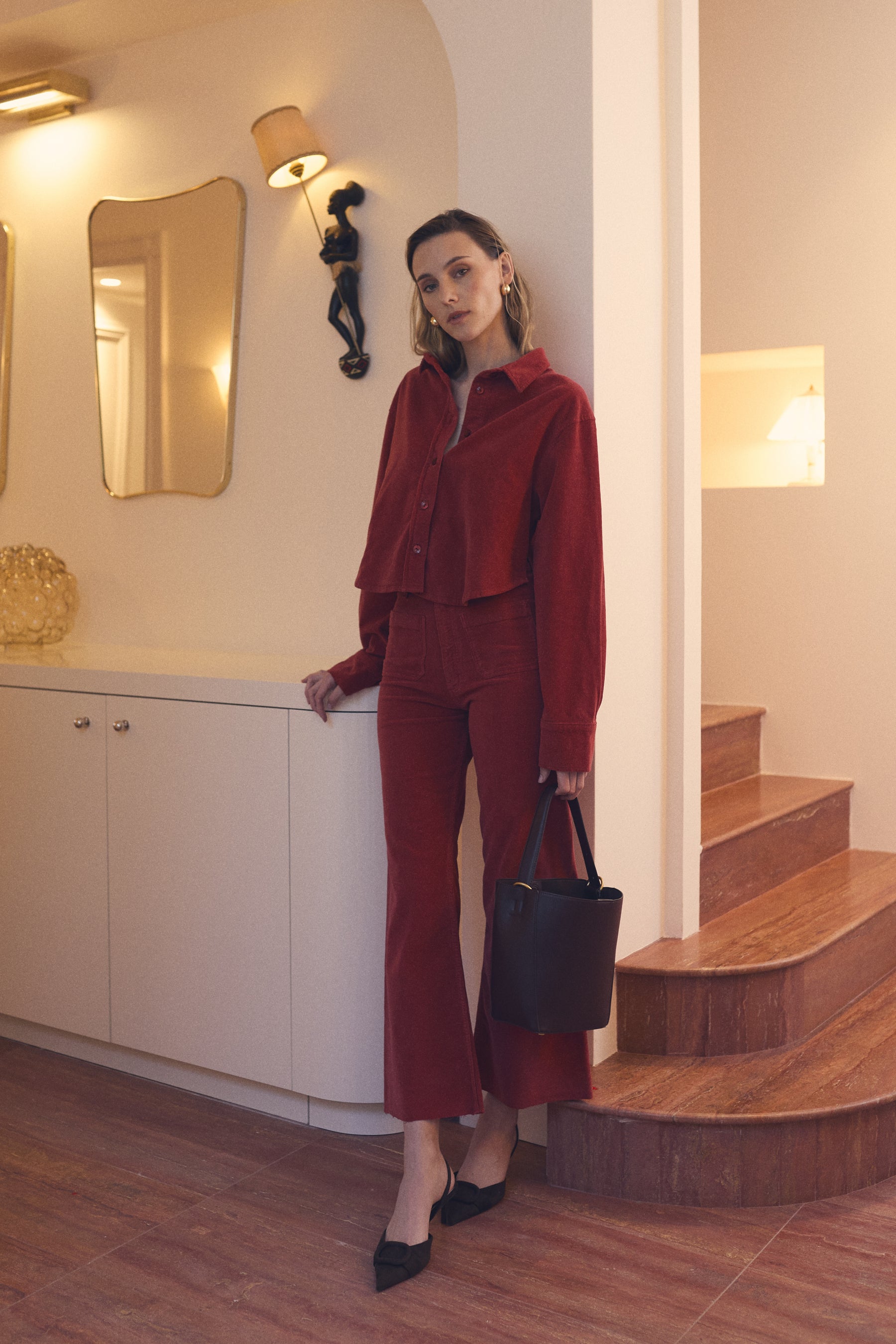Woman in a red outfit standing in a room with wooden steps and decorative elements.