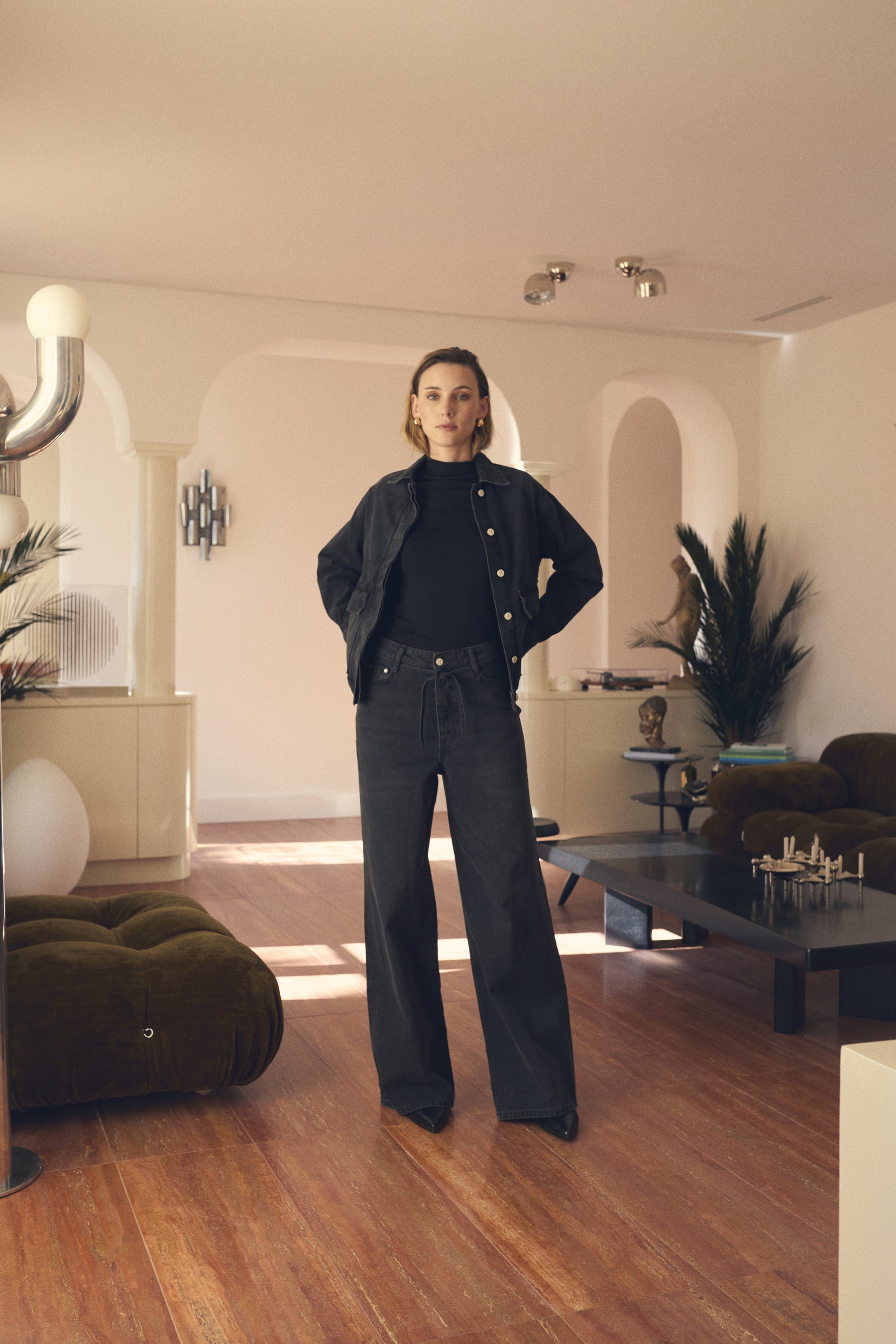 Person standing in a modern living room with wooden floors and decorative elements.